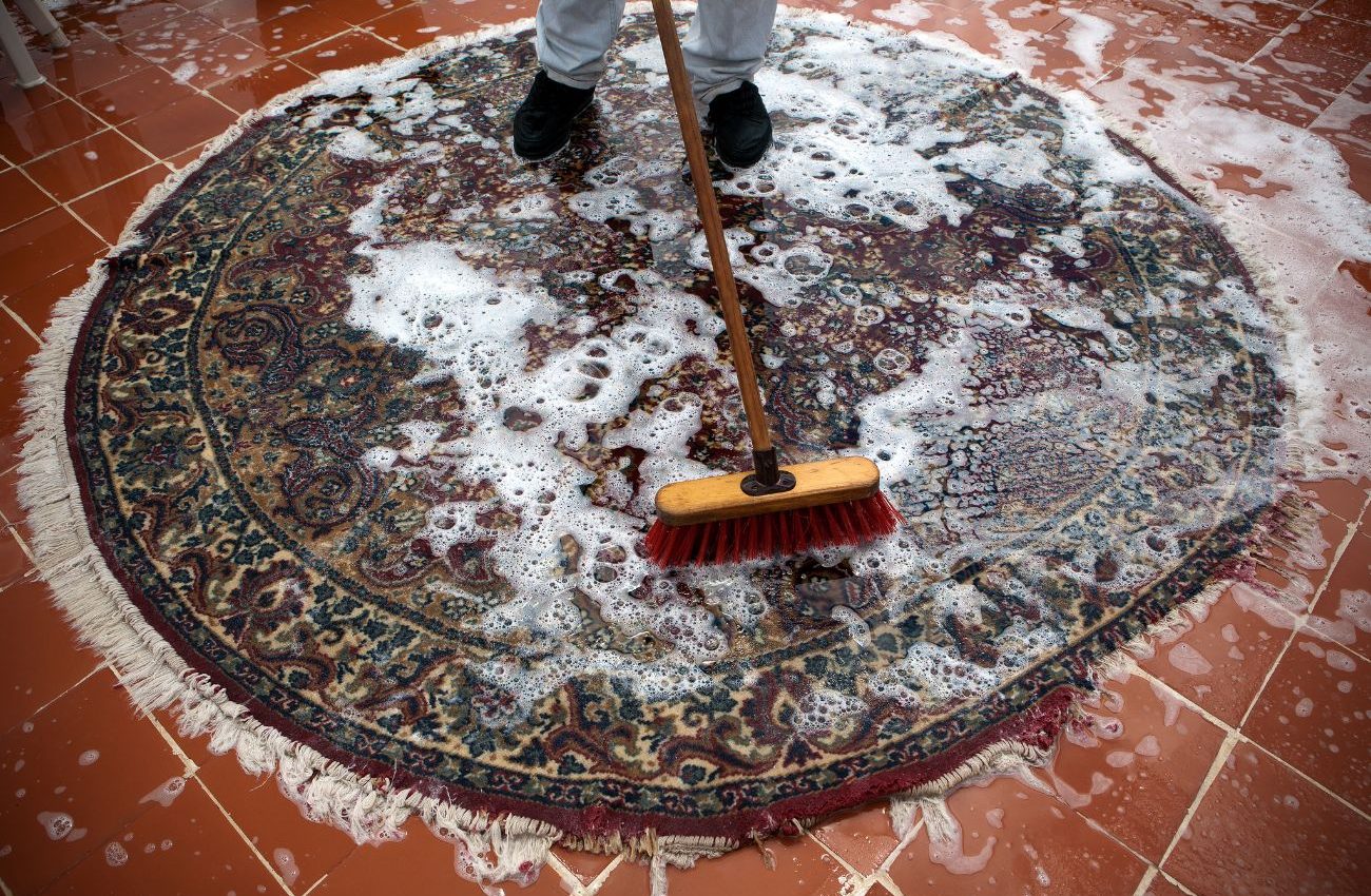 A person cleaning a rug with a broom, showcasing a carpet cleaning service located in Jacksonville, FL.