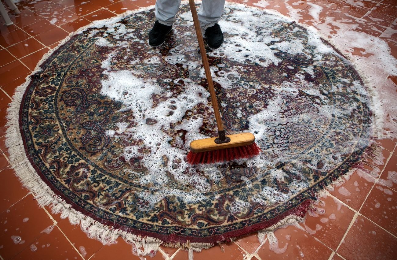 A person cleaning a rug with a broom, showcasing a carpet cleaning service located in Jacksonville, FL.