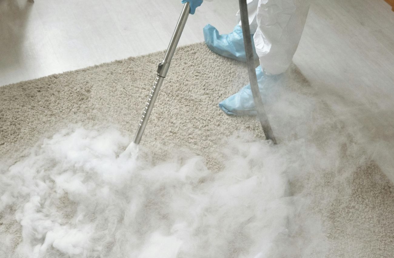 A person in white clothing operates a steam cleaner on a carpet, showcasing a Jacksonville, FL cleaning service.