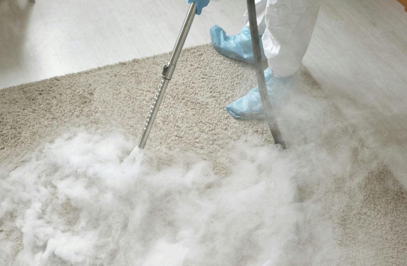 A person in white clothing operates a steam cleaner on a carpet, showcasing a Jacksonville, FL cleaning service.
